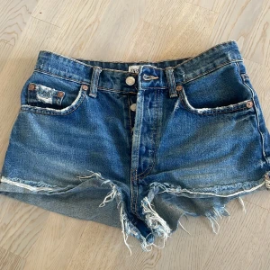Blå denimshorts från ZARA med fransar - Snygga blå denimshorts från ZARA med råa, fransiga kanter och klassisk femficksmodell. Shortsen har låg midja och slitna detaljer för en cool, avslappnad look. Perfekta till sommaren och lätta att matcha med allt.