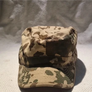 Camo keps i militärstil - Säljer en keps i klassisk militärstil med camouflage-mönster i beige, brunt och grönt. Kepsen har platt ovandel och rak skärm, tillverkad i slitstark bomull. Perfekt för dig som gillar outdoor eller vill ha en streetig look.