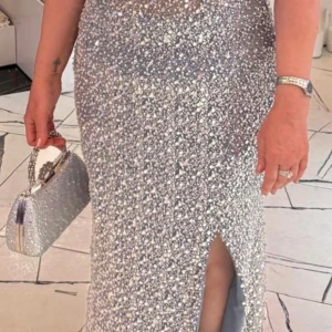Glittrig silver långklänning med slits - Superglittrig långklänning i silver med en snygg slits framtill. Klänningen är täckt av paljetter som ger en maxad festkänsla och har en figurnära passform. Perfekt för dig som vill sticka ut och glänsa på festen. Storleken är 46 men passar mer som en storlek 44