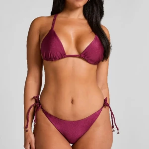 Vinröd bikini med knyt och snörning - Fin vinröd/lila bikini sett med massor av snygga detaljer. Helt nytt utan att  ha provat den. Fick hem fel storlek och kan ej skicka tillbaka, så hoppas den kan passa nån annan! Storlek M i bhn och S i trosorna. Nypris 648kr (skickas även i original förpackning)