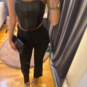 Svarta kostymbyxor med rak passform - Snygga svarta kostymbyxor med hög midja och rak passform. Byxorna har klassiska fickor fram och bak, stängs med knapp och dragkedja. Perfekta för en stilren look och passar till många olika outfits.