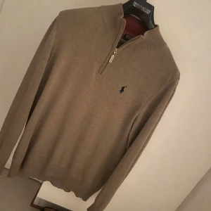 Beige half zip tröja Polo Ralph Lauren - Säljer en beige långärmad tröja från Polo Ralph Lauren med half zip och broderad logga på bröstet. Tröjan har ribbad krage och är tillverkad i mjukt material som passar perfekt till höst och vinter. Klassisk och stilren modell. Perfekt för lager på lager. Pris kan diskuteras