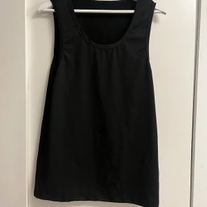 Svart ärmlös linnetopp - En stilren svart linnetopp med rund halsringning och rak passform. Toppen är helt slät utan mönster eller detaljer och är perfekt för att skapa en clean look. Materialet känns lätt och passar bra till många olika outfits.