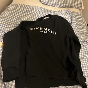 Svart Givenchy sweatshirt med tryck - Svart sweatshirt från Givenchy med vit logotyptext 'GIVENCHY PARIS' på bröstet. Klassisk rund halsringning och långa ärmar. Mjuk insida och stilren design som passar perfekt till jeans eller joggers.