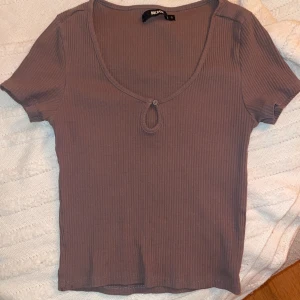 Tshirt - Ribbad brun topp från Bik Bok med korta ärmar och en liten detalj framtill vid halsringningen (Se bild 2). Bra passform och bra skick. Strl S men passar också som XS (ganska tajt). Till naveln. Kontakta för mer info/ fler bilder. 
