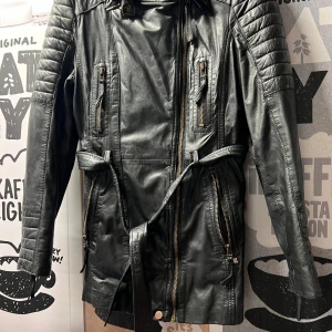 Skinnjacka - Svart jacka i mjuk läder, knappt använd. Storlek 38-40. Märke Freaky Nation, köpt på Zalando för 1800kr. Många fickor ( en innerficka). Dragkedja i ärmsluten.  Fin rutig foder i bomull och andra fina detaljer, skärp mm. Säljs pga viktuppgång. Längd 75 cm Finns i Liljeholmen.