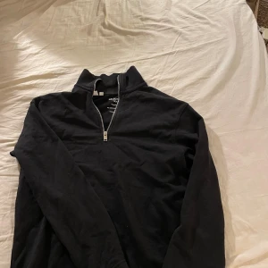 Svart half zip-tröja från Selected Homme - Svart långärmad tröja från Selected Homme med half zip-dragkedja i halsen. Tröjan har en hög krage och är gjord i mjuk bomull, perfekt för lager-på-lager och chill vardagsstil.