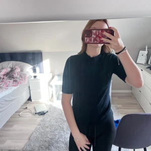 Svart stickad topp med kort ärm - En svart stickad topp med korta ärmar och rund hals. Modellen är enkel och stilren, perfekt att matcha med både jeans och kjol. Materialet är mjukt och följsamt, vilket gör den skön att bära hela dagen.