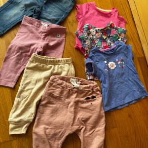 Klädpaket flicka - Fyra par mjuka barnbyxor: ett par rosa leggings, ett par beige mjukisbyxor med resår i midjan, ett par jeans och ett par ljusrosa byxor med knyt och söt broderad detalj framtill. Perfekta för lek och vardag, tillverkade i bomull för extra komfort. Kläderna är mellan storlek 56-68