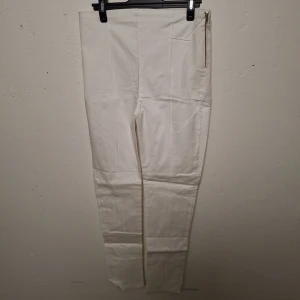 Vita slim byxor med dragkedja - Snygga vita byxor med smal passform och hög midja. Byxorna har en guldig dragkedja i sidan och markerade sömmar längs benen. Perfekta för dig som gillar en clean och stilren look. Materialet känns som bomull eller polyester.