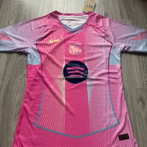 Barça x Nike rosa fotbollströja  - Säljer en officiell FC Barcelona fotbollströja från Nike i rosa och ljusblått med gult Nike-märke och klubbmärke på bröstet. Tröjan har korta ärmar, V-ringning med turkos kant och är tillverkad i lätt Dri-FIT-material. Spotify-logga på magen och unikt grafiskt mönster.