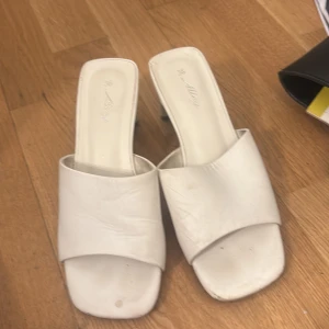 Vita klackade sandaler från Alley - Snygga vita sandaler från Alley med fyrkantig tå och bred rem över foten. Skorna har en låg klack och är tillverkade i syntetmaterial. Perfekta för dig som gillar minimalistisk och trendig stil. Har lite smuts fläckar men går o få bort med lite puts!