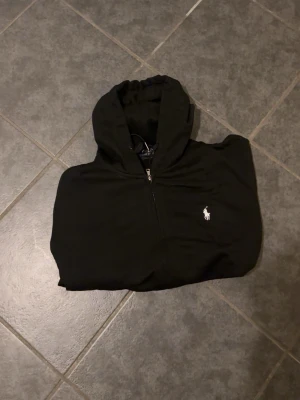 Svart Ralph Lauren hoodie - Svart Ralph Lauren hoodie med vit logga. Helt oanvänd så den är i perfekt skick 