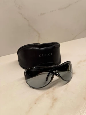 Svart solglasögon från Gucci - Säljer ett par snygga svarta solglasögon från Gucci med metallbågar och mörka glas. Medföljer ett svart fodral i skinn med Gucci-logga. Perfekt accessoar för dig som vill ha en lyxig och stilren look.