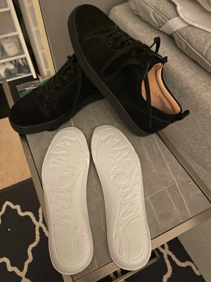 Svarta sneakers från Christian Louboutin - Säljer ett par svarta sneakers från Christian Louboutin i mocka med svarta snören och rund tå. Skorna har beige innersula i skinn med logotyp och Paris-tryck. Medföljer även extra innersulor med präglad text. Riktigt clean och stilren modell. Har används två gånger och tyvärr gick skolådan sönder. Pris kan diskuteras 