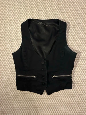 Svart och silvrig kostymväst - Suppersnygg svart kostymväst med silvriga kedjor. Skjusterbar där bak. Har endast västen till fest eller över en skjorta till vardags. Bra skick!