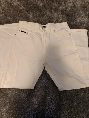 Vita raka byxor från Hugo Boss i storlek 34 - Säljer ett par stilrena vita byxor från Hugo Boss med klassisk femficksdesign och raka ben. Byxorna är i storlek 34. Byxorna har en snygg svart patch med logga bak i midjan och är tillverkade i mjuk bomull. Perfekta för dig som vill ha en clean och fräsch look.