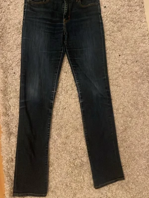 Levis  mörkblå jeans - Säljer ett par mörkblå slim Levis jeans med klassisk femficksdesign och diskreta slitningar framtill. Jeansen har en smal passform som sitter snyggt längs benen och är tillverkade i tåligt denimtyg. Mycket bra skick men har sytt till egna fickor. 