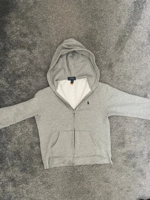 Grå tröja från Ralph Lauren - Grå snygg Ralph Lauren tröja med ett mörkt blått märke på bröstet. Det står att det är storlek 14-16 men jag skulle säga mer att det är storlek 146-152