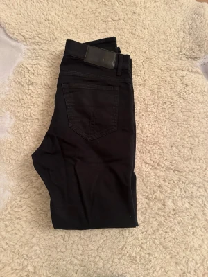 Svarta Tiger of Sweden jeans - Säljer ett par svarta jeans från Tiger of Sweden. De har en klassisk femficksmodell, raka ben och normal passform. Materialet är mjukt och stretchigt jeans-tyg som sitter snyggt. Perfekta till en clean och stilren look.