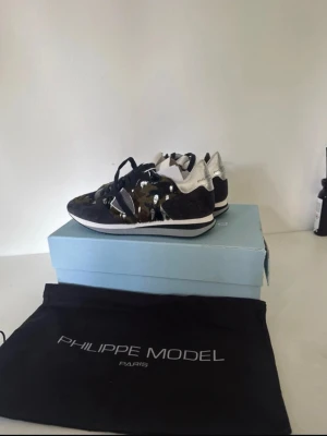 Philippe Model sneakers camo silver - Säljer ett par Philippe Model TRPX Low sneakers i storlek 36. Skorna har en unik camouflagemönstrad ovandel i pony hair, svarta och gröna toner samt detaljer i silver på hälen. Klassisk snörning och platt sula för skön vardagsstil. Kommer med originalpåse och låda.