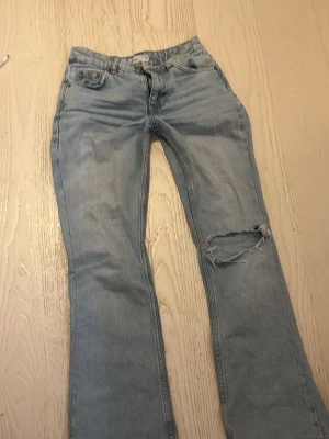 Ljusblå jeans från Gina Tricot - Ljusblå jeans från Gina Tricot med klassisk femficksmodell och slitning med hål på ena knät. Jeansen har rak passform och normal midja. Tillverkade i bomull med dragkedja och knapp framtill. Perfekta för en avslappnad och trendig look.