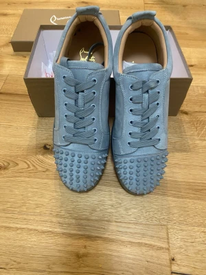 Blå mocka sneakers från Louboutin - Säljer ett par sjukt snygga blå sneakers från Christian Louboutin i mocka. Skorna har coola nitar på tån, klassisk snörning och den ikoniska röda sulan. Insidan är i beige skinn och de har en clean, modern look som sticker ut.