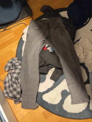 Grå jeans med smal passform - Säljer ett par grå jeans med klassisk femficksdesign och smal passform. Jeansen har en enkel look utan synliga detaljer och är perfekta för dig som gillar stilrena basplagg. Materialet är jeans och färgen är en snygg mellangrå nyans.