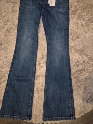 Bootcut jeans Gina Tricot strl 38 - Blå bootcut jeans från Gina Tricot i storlek 38. Low waist, bootcut med lite utsvängda ben. Femficksmodell och knappgylf.