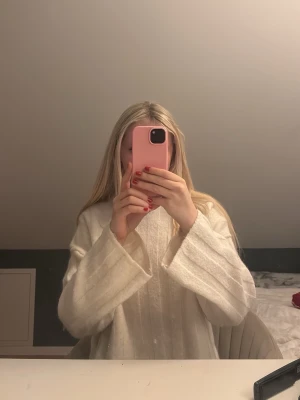 Vit stickad långärmad tröja - Mysig vit stickad tröja med breda ärmar och diskreta lodräta ränder. Perfekt för kyligare dagar och enkel att matcha med olika outfits. Snygg och stilren design som passar till många tillfällen.