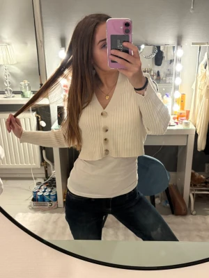 Vit ribbad kofta med knappar - Säljer en kort, ribbad kofta i vit färg med v-ringning och stora dekorativa knappar framtill. Koftan har lång ärm och är croppad i modellen, perfekt att slänga över ett linne eller t-shirt. Enkel och stilren design som man kan ha till precis allting.❣️