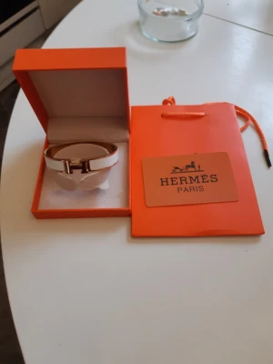 Hermes armband  - Bilderna visar ett Hermès-armband i originalförpackning, men ingen väst syns. Kan därför inte ge någon beskrivning av väst.