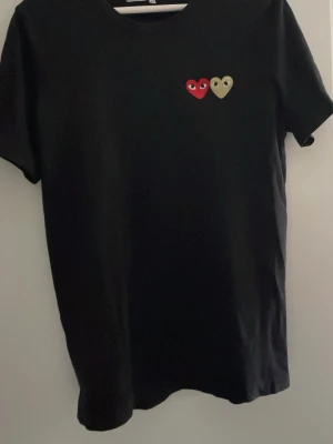 Comme des Garçons Play t-shirt - Svart t-shirt från Comme des Garçons Play med två broderade hjärtan på bröstet, ett rött och ett beige. Klassisk rund halsringning och korta ärmar.  Storlek M, sitter bra på M