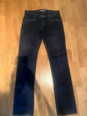 Mörkblå Acne Jeans 30/34 straight fit - Säljer ett par mörkblå Acne Jeans i rak modell. Klassisk femficksdesign, tillverkade i 100% bomull. Snygg tvätt med subtila slitningar och metallknapp framtill. Perfekta för dig som gillar stilrena och tidlösa jeans.