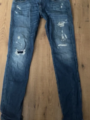 Replay Anbass blå slitna jeans - Säljer ett par Replay Anbass jeans i blå tvätt med slitningar och hål på benen för en riktigt avslappnad look. Skinny fit med klassiska fem fickor och dragkedjegylf. Perfekta för dig som gillar en trendig och casual stil.