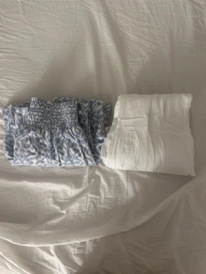 3-pack kjolar i olika färger och stilar - Säljer tre kjolar: en blåvit mönstrad kjol från 157 med smock i midjan, en vit kjol från Gina Tricot med smockdetaljer och en beige långkjol i mjukt, glansigt material. Perfekta för sommardagar och lätta att matcha med olika toppar.