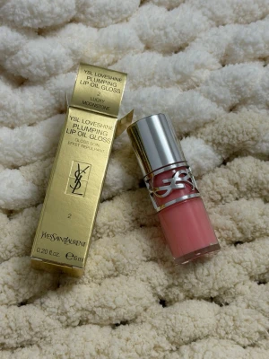 YSL Loveshine Plumping Lip Oil Gloss - YSL Loveshine Plumping Lip Oil Gloss i färgen 2 Lucky Moonstone. Kommer i en lyxig guldfärgad förpackning och har en snygg rosa ton. Hylsan är genomskinlig med silverdetaljer och YSL-logga. Innehåller 6 ml och ger glansiga, fylliga läppar.