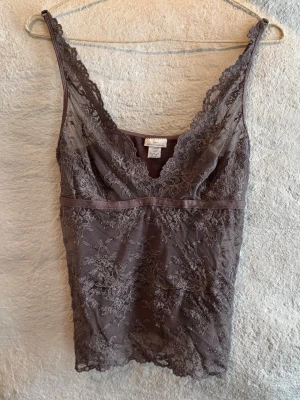 Brun spetslinnetopp från DAY - Säljer en brun super fin linnetopp från DAY Birger et Mikkelsen med vacker spets framtill och längs kanterna. Toppen är väldigt strechig vilket gör att den passar storlek S-L. Den har smala axelband som går att ljustera, v-ringning och transparent spetsdetalj över bröstet. 