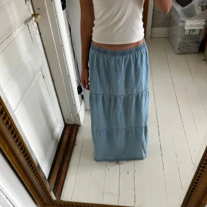 Ljusblå långkjol med resårmidja - Luftig och skön ljusblå långkjol med resår i midjan och volangliknande sömmar. Kjolen har en avslappnad passform och är tillverkad i mjuk bomull, perfekt för varma dagar. Enkel att styla med crop top eller linne.