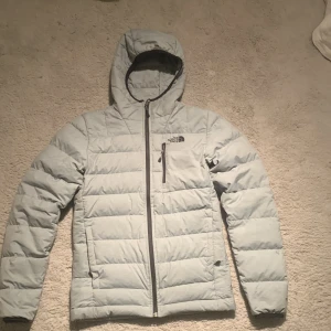 Ljusgrå dunjacka från The North Face XS - Säljer en ljusgrå dunjacka från The North Face i storlek XS. Jackan har huva, dragkedja framtill och en bröstficka med dragkedja. Quiltad design och klassisk logga på bröstet. Perfekt för vintern. Och riktigt snygg. Kan även användas som skidjacka. Defekter på dom 2 sista bilderna.