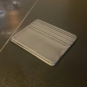 Grå kortfodral i skinn - Slimmat grått kortfodral med plats för flera kort, tillverkat i slätt skinn. Stilren och enkel design med raka linjer och synliga sömmar. Perfekt för dig som vill ha koll på korten utan att ta upp mycket plats i fickan eller väskan.