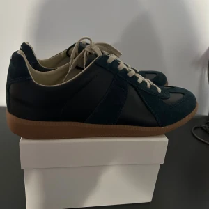 Maison Margiela sneakers blå mocka - Maison Margiela sneakers i mörkblå mocka och svart skinn med beige snörning och innersula. Skorna är i 10/10. Skorna är storlek 43 och dem har inga defekter. Kvitto finns 