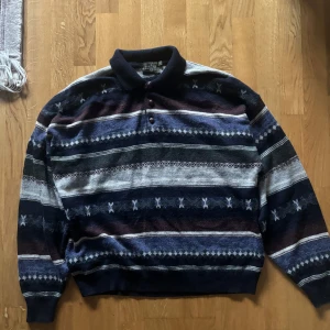 Randig stickad  pikétröja från West Point - Vintage pikétröja från West Point med krage och knappar. Tröjan har ett randigt mönster i mörkblått, grått, vinrött och grönt. Långärmad och stickad i mjukt material, perfekt för höst och vinter. Snygg retrostil med relaxed fit.