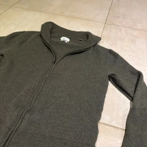 These Glory Days kofta - Säljer en olivgrön kofta från These Glory Days i mjuk och lyxig merinoull. Koftan har hel dragkedja framtill, ribbade muddar och en stilren, enkel design. Det är storlek XL men den har krympt så den är ungefär som XS. Kan ha tappat formen lite men inte helt säker då den inte passar mig. Sista bilden är en gammal bild innan den krympte.