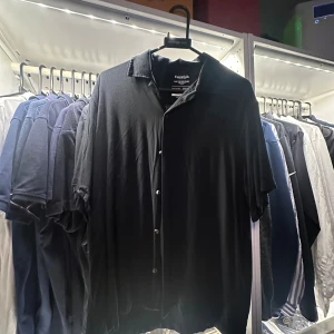 Svart cubansk skjorta från Essentials - Svart skjorta med cubansk krage från Essentials by Jack & Jones. Tillverkad i mjuk viskos som ger en skön och luftig känsla. Skjortan har korta ärmar och knappar framtill, perfekt för en chill och stilren look.