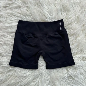 Svarta träningstights-shorts från DFYNE - Säljer ett par svarta, tighta träningstights-shorts från DFYNE. De är högmidjade med bred resår i midjan och har en stilren design utan synliga sömmar framtill. Perfekta för gymmet eller löpning. Storlek L men sitter som M.