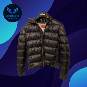 Parjumper pufferjacka svart - Svart pufferjacka från Parajumpers, modell Sheen. Jackan har en glansig finish, huva, ribbade muddar och dragkedja framtill. Klassisk Parajumpers-patch på ärmen och quiltad design. Perfekt för kalla dagar och riktigt snygg streetstil. Använd ett flertal gånger men fortfarande i jätte bra skick, Y-M motsvarar S och jag är 172 på mig sitter den parfekt till midjan och armar 