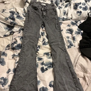 Grå bootcut jeans med hög midja - Snygga grå jeans med bootcut-modell. Klassisk femficksdesign och dragkedja med knapp framtill. Jeansen har en cool tvättad look och är perfekta för dig som gillar en avslappnad men trendig stil. Deras perfect jeans modell