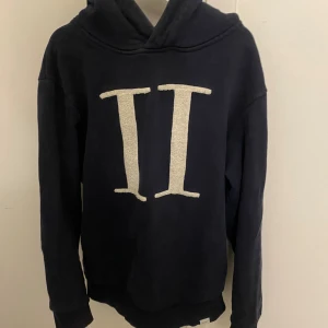 Mörkblå hoodie från Les Deux - Säljer en mörkblå hoodie från Les Deux med stor vit II-logga framtill. Tröjan har huva, långa ärmar och är tillverkad i mjukt material som känns riktigt skönt.