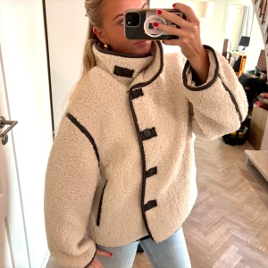 Vit teddyjacka med svarta detaljer - Säljer denna skitsnygga eftertraktade vita/ljusbeigea teddyjacka med svarta/mörkbruna kantdetaljer från H&M. Endast använd ett fåtal gånger och är därför i väldigt fint skick 🩷